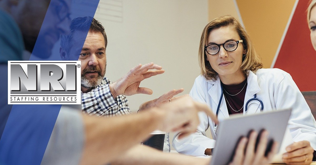 a female Dr with blonde hair is in a meeting and looking at a tablet while 2 men and another female healthcare worker look on