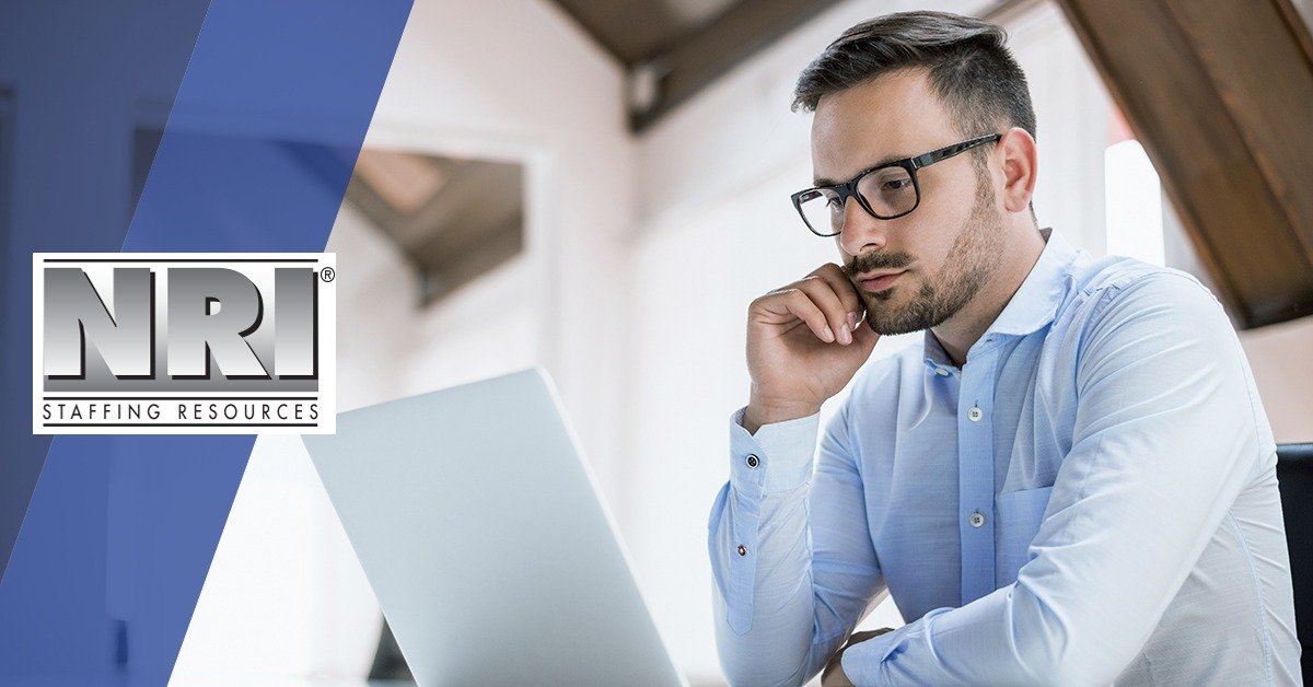 A white male wearing glasses and a while button down shirt is deep in thought and looking at a laptop screen