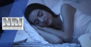 a Caucasian woman with dark hair is sleeping peacefully on her side in bed