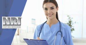 A female Caucasian is wearing light blue scrubs with a stethoscope around her neck. She is holding a clipboard and smiling.