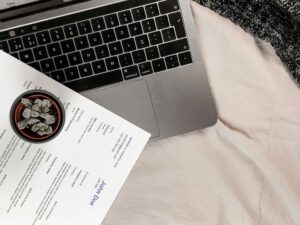 Laptop and resume on a desk with a potted plant, symbolizing skills to list on a resume, job searching, and professional career development.