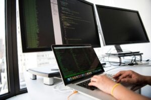 Professional working on code across multiple screens, representing IT entry level jobs in a modern tech workspace.