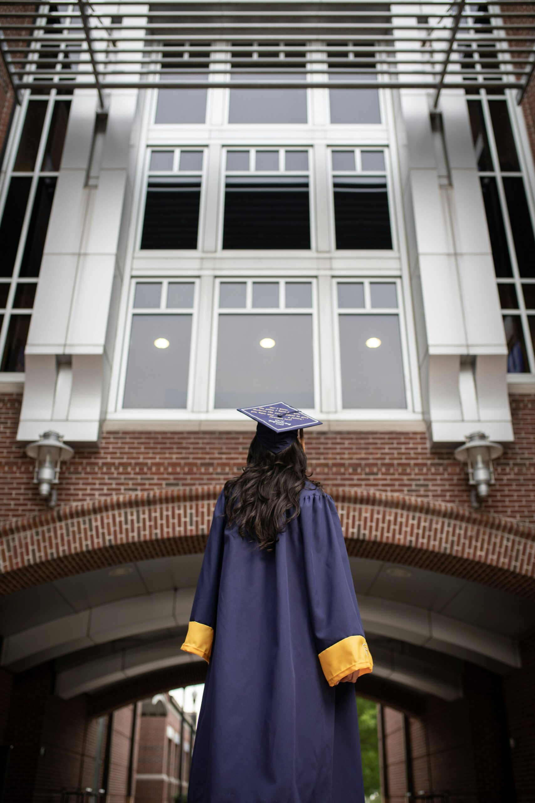 Recent college graduate in cap and gown facing campus building, considering first job out of college staffing agency options.