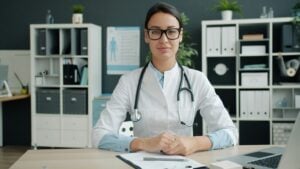 healthcare administrative assistant skills — medical office professional smiling at front desk in a busy healthcare facility