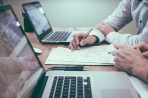 401k first job new graduate — two professionals reviewing retirement plan documents and financial paperwork at a desk with laptops