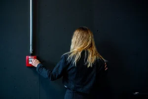 A person activating a red fire alarm pull station — when systems trigger, fire watch keeps a property covered.